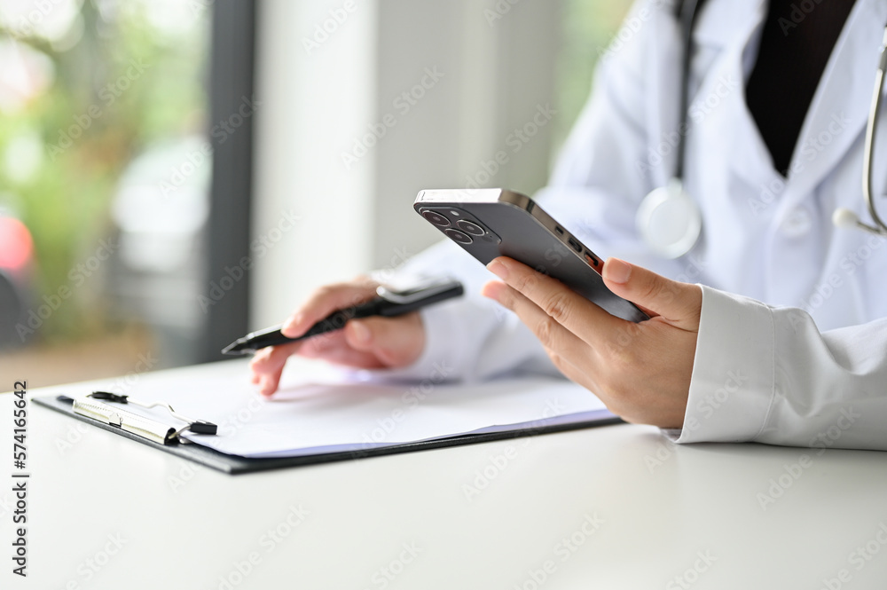 Fototapeta premium Cropped image of a professional Asian female doctor using her smartphone at her desk.