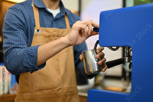 Cropped image of a barista in apron steaming fresh milk with espresso machine  working in cafe.