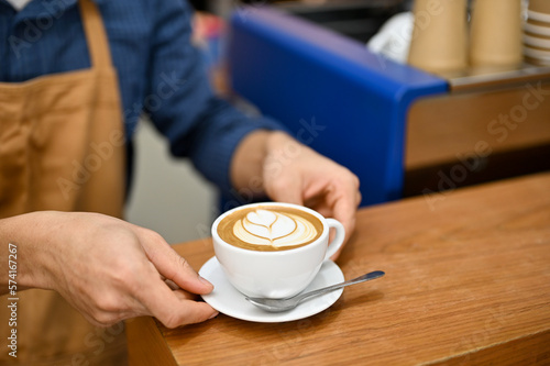 Close-up image of a barista serving a beautiful latte on wood table. food and drink concept