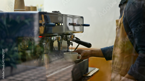 Male barista or bartender in the coffee shop making cappuccino with espresso machine