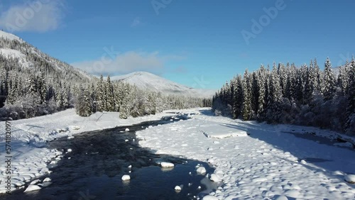 cold river tream with snow and sunshine surrounded by forest, aerial video photo