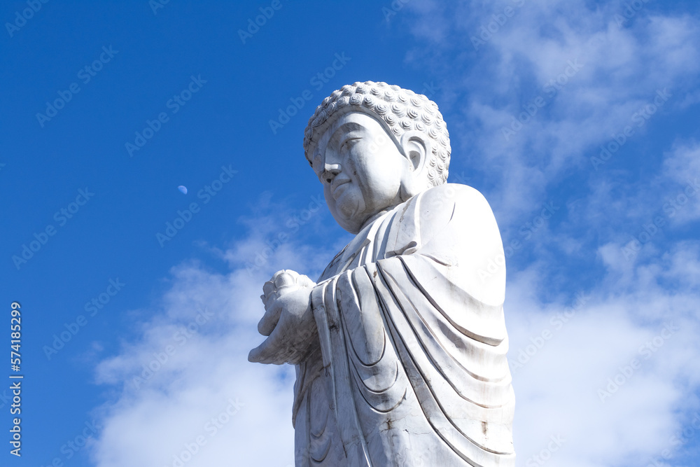 white statue of Buddha in old town in Jiamusi, city of china, visible moon in background blue sky. 