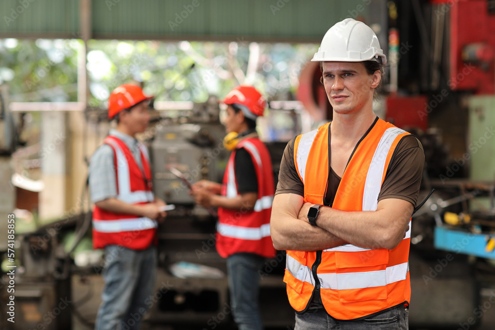 Technician engineer in protective uniform standing and using walkie talkie radio while controlling operation or checking industry machine process with hardhat at heavy industry manufacturing factory Technician engineer in protective uniform standing and using walkie talkie radio while controlling operation or checking industry machine process with hardhat at heavy industry manufacturing factory