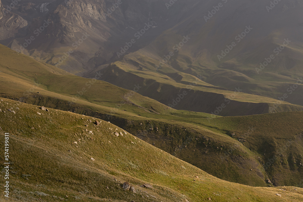 Sunny yellow and green mountain valley with velvety hilly slopes in golden sunlight with deep clefts, shadows, light mist on sunset in summer, detail. Mountain landscape, adventure in Dagestan.