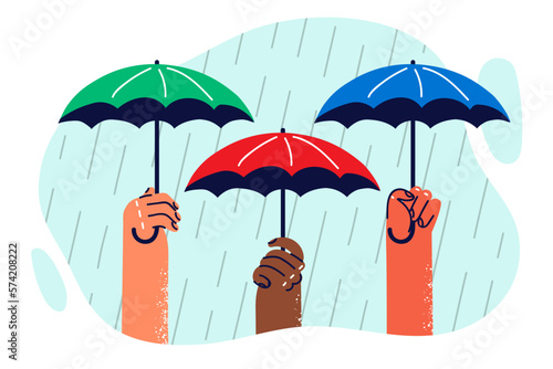Hands of people with umbrellas protecting from heavy rain symbolizing onset of autumn