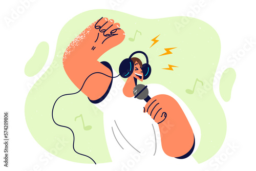 Positive man in headphones holding microphone enjoying singing in karaoke club while relaxing
