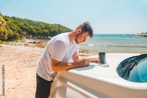 man checking on map at car hood destination place sea beach on background