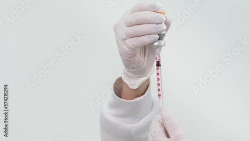An unrecognizable doctor fills a syringe with a vaccine or other medicine on a light background. A professional nurse in gloves and uniform prepares a drug photo