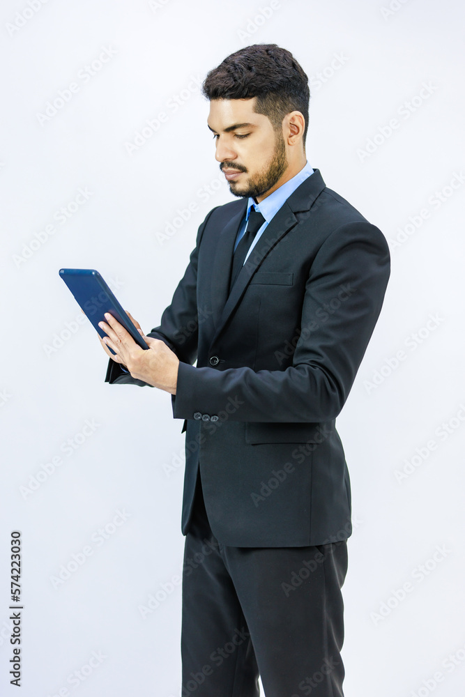 Millennial Asian Indian young professional successful bearded male businessman in formal business suit standing holding using touchscreen tablet computer working online with client on white background Millennial Asian Indian young professional successful bearded male businessman in formal business suit standing holding using touchscreen tablet computer working online with client on white background