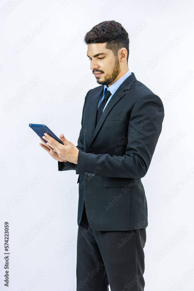 Millennial Asian Indian young professional successful bearded male businessman in formal business suit standing holding using touchscreen tablet computer working online with client on white background Millennial Asian Indian young professional successful bearded male businessman in formal business suit standing holding using touchscreen tablet computer working online with client on white background