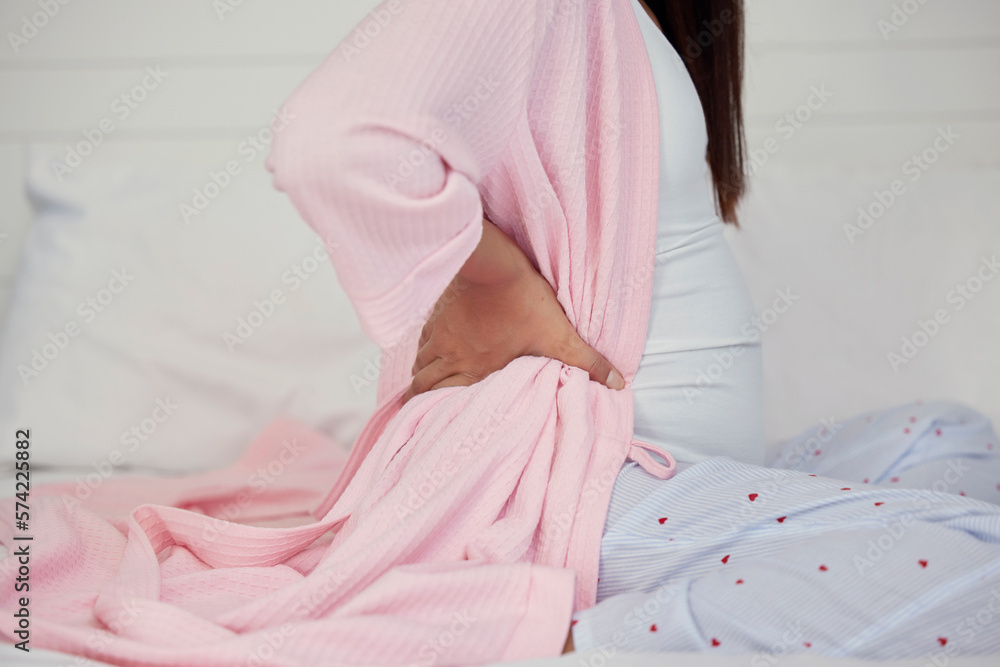 Tired, healthcare and pregnant woman with back pain on a bed for rest, break and maternity leave