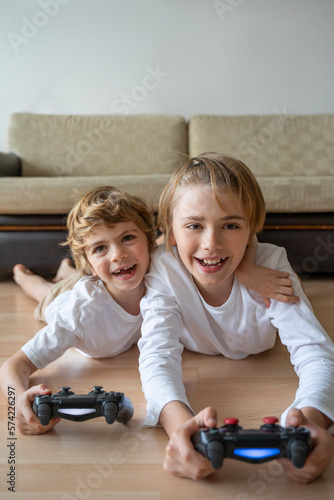 Cute children joyful playing video games with controller console, brother sister expressing emotions while enjoying their hobby playstation joystick. Vertical