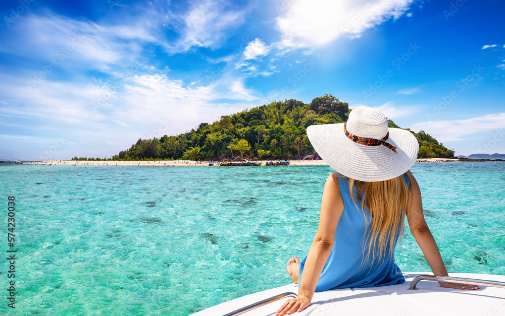 A beautiful tourist woman with sunhat sits on a yacht and looks at the turquoise sea and beaches of Bamboo island in the Krabi region, Thailand - obrazy, fototapety, plakaty 