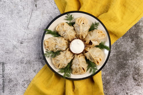 Manti steamed Dumplings with meat and potatoes with sauce and herbs on a round plate on a dark gray background. Top view, flat lay