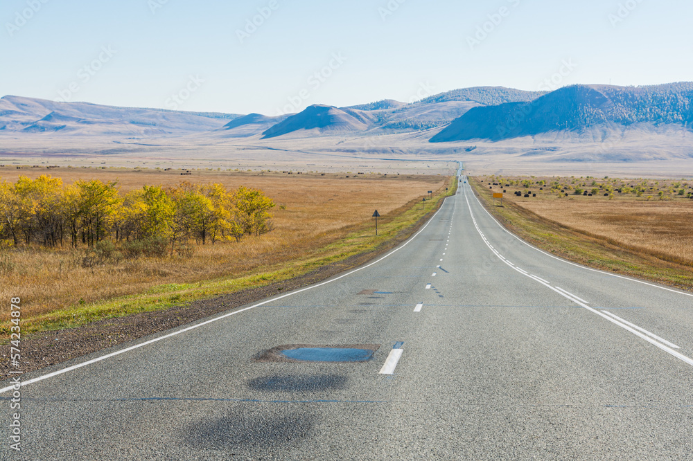 An asphalt road runs through the steppe. Autumn. Hills are visible in the distance