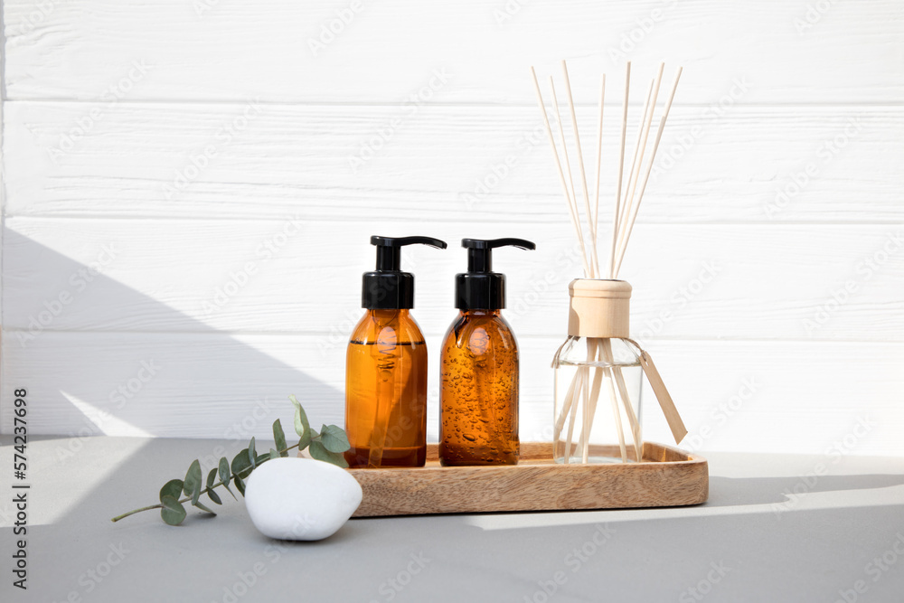 Obraz premium Amber bottles with facial cosmetics on a tray and aroma diffuser with a branch of eucalyptus on the wooden background. Front view