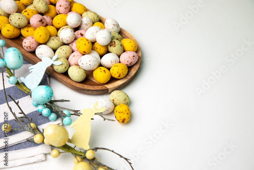 Multi-colored chocolate decorative eggs in wooden tray on a white background with decorative branches. Happy Easter background. Flat lay