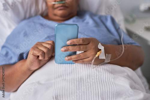 Close up of black woman holding smartphone while laying on bed in hospital