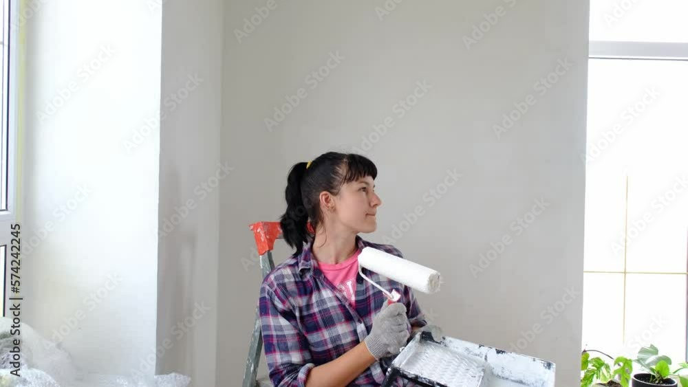 puzzled woman in paint roller and white paint for walls in hands close-up portrait. Construction work and cosmetic repairs in house, wall painting, tinting, finishing work with your own hands puzzled woman in paint roller and white paint for walls in hands close-up portrait. Construction work and cosmetic repairs in house, wall painting, tinting, finishing work with your own hands