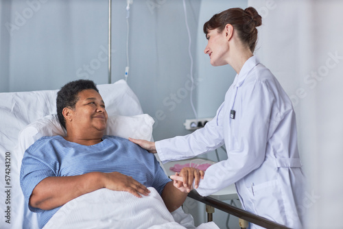 Portrait of African American senior woman on hospital bed with young nurse supporting her