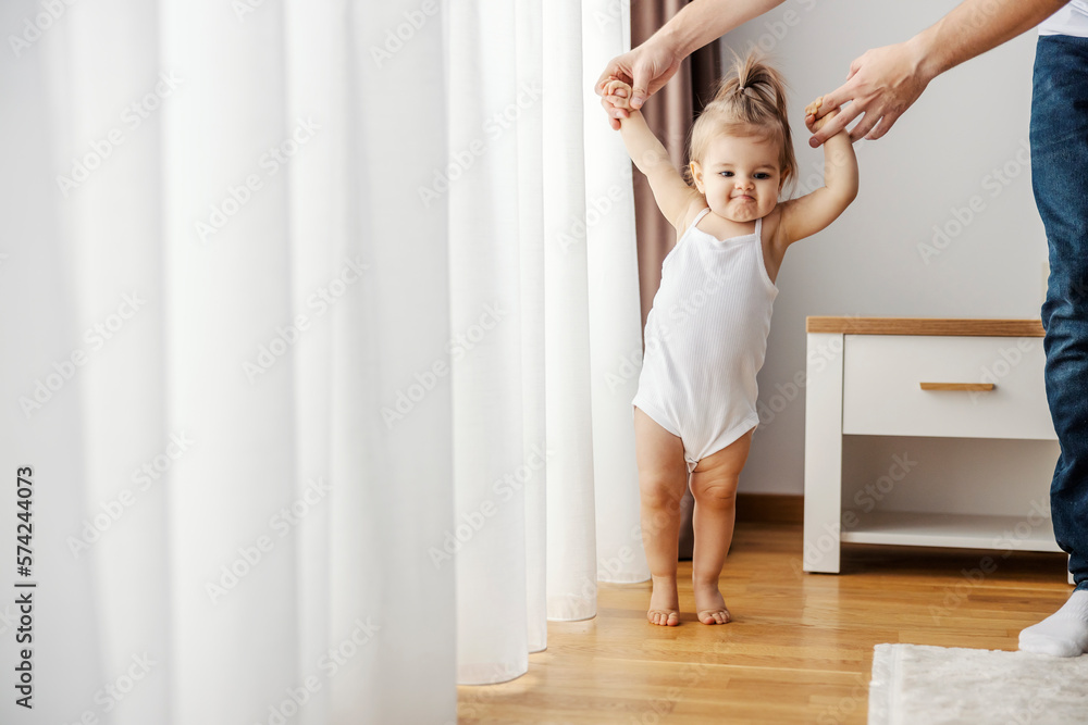 A baby girl is learning how to walk with a little help of her father. A baby girl is learning how to walk with a little help of her father.