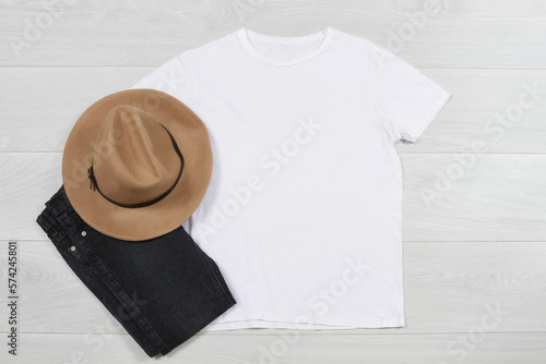 White T-Shirt mockup. Template blank shirt top view on white wooden background. Spring summer outfit on wood floor. Woman fashion clothes. Autumn look of today. Female Jeans, hat accessories