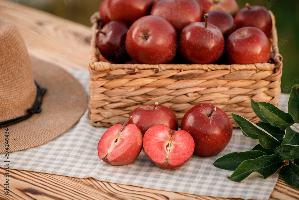Fresh ripe red apples in the basket on wooden table with natural orchard background. Vegetarian fruit composition. Harvesting concept Fresh ripe red apples in the basket on wooden table with natural orchard background. Vegetarian fruit composition. Harvesting concept