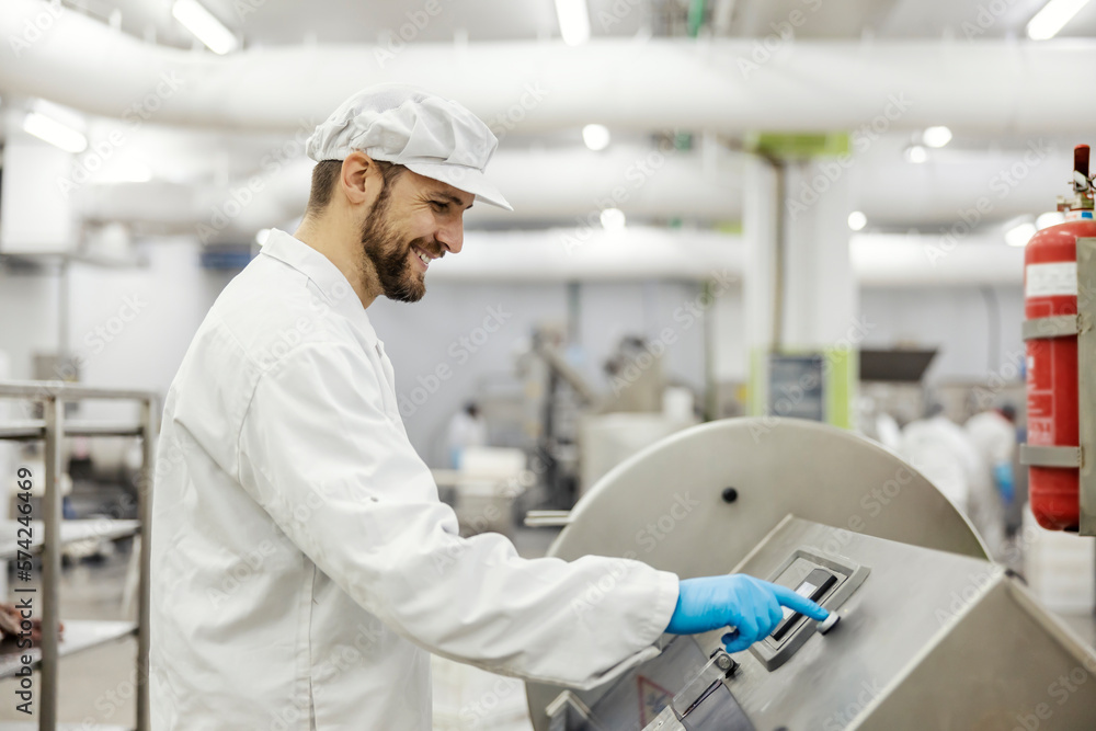 A smiling meat industry worker is pressing start button on a meat processing machine. A smiling meat industry worker is pressing start button on a meat processing machine.