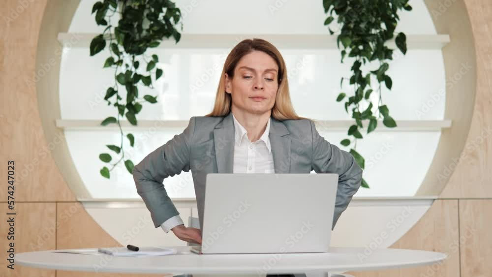 Backache. Tired unhealthy female worker in formal suit touching injured sore back, suffering lower lumbar discomfort, muscle pain of overwork, pinched nerve Woman sitting at office desk having injury. Backache. Tired unhealthy female worker in formal suit touching injured sore back, suffering lower lumbar discomfort, muscle pain of overwork, pinched nerve Woman sitting at office desk having injury.