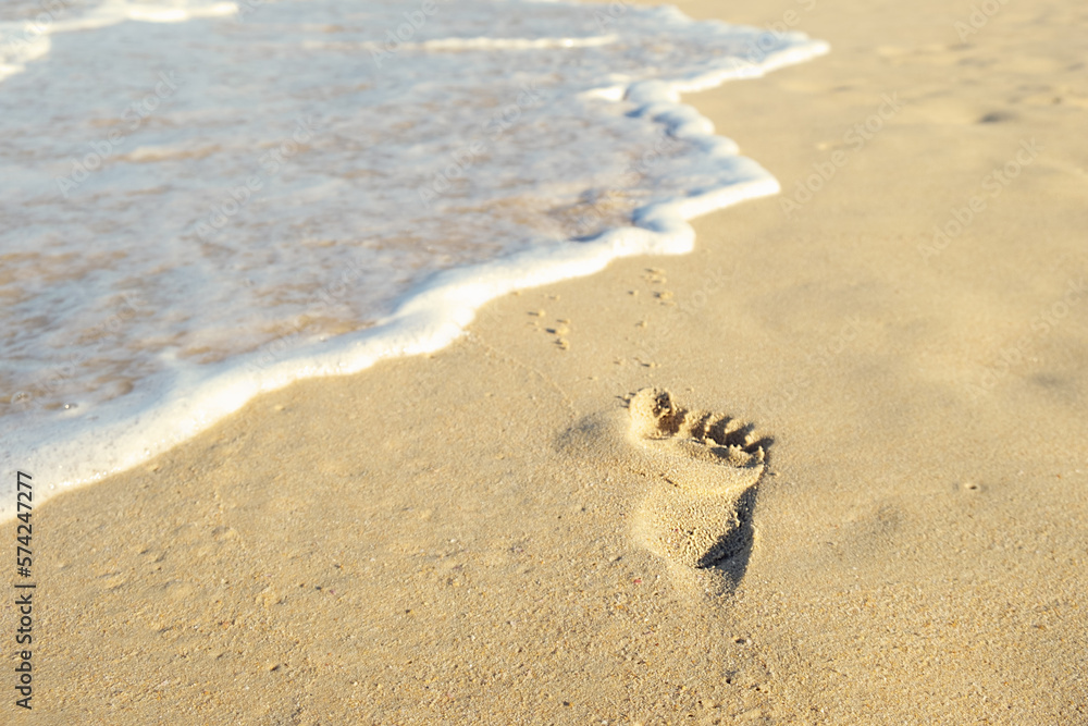 Sea waves wash away footprints of a barefoot man on a sandy beach at the water's edge. Man was walking along beach along the sea and left footprints. Concept of summer holidays, walks along the coast Sea waves wash away footprints of a barefoot man on a sandy beach at the water's edge. Man was walking along beach along the sea and left footprints. Concept of summer holidays, walks along the coast