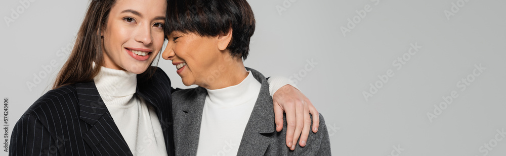 happy woman in black jacket hugging asian mother and smiling at camera isolated on grey, banner happy woman in black jacket hugging asian mother and smiling at camera isolated on grey, banner