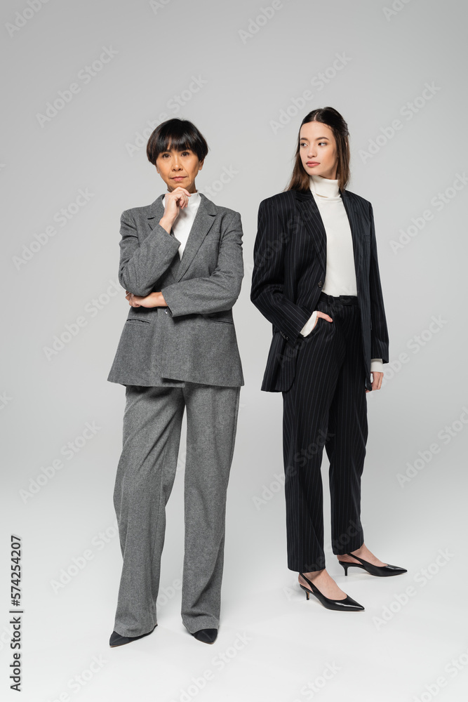 full length of middle aged asian woman with stylish daughter posing on grey background full length of middle aged asian woman with stylish daughter posing on grey background