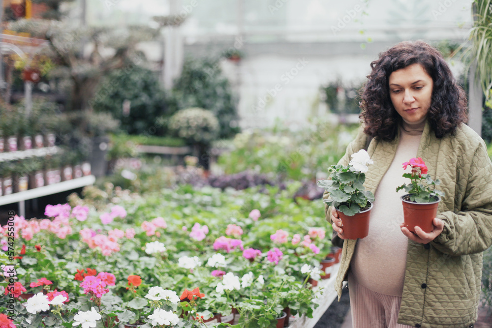 Pregnant woman in green jacket choosing a flower plant in a plant shop