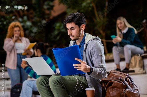 Portrait of male student siting in campus using laptop.