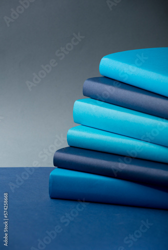 Stack of books Different tones of blue, on desk, with gray background