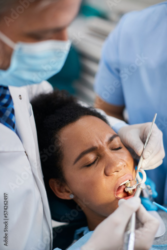 Black woman holds her eyes closed during dental procedure at dentist s office.