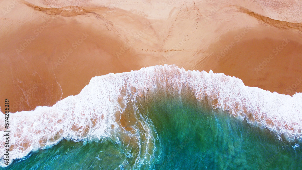 Aerial view of the waves with foam on the sandy ocean shore. Beautiful texture background for tourism and design. Tropical seashore