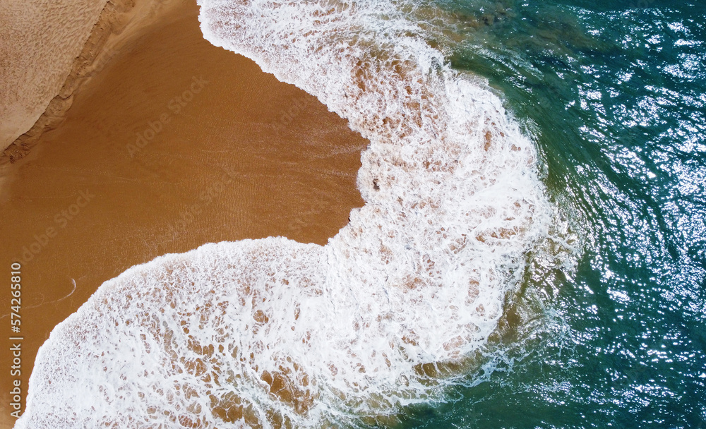 Aerial view of the waves with foam on the sandy ocean shore. Beautiful texture background for tourism and design. Tropical seashore