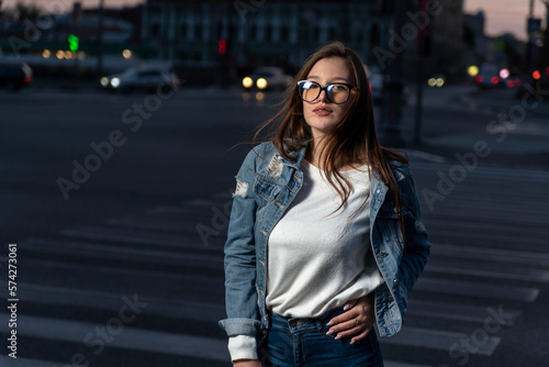 Stylish young woman in glasses on city street, summer time. Portrait of brunette girl in youth clothes on evening city