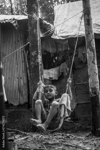 Little Bangladeshi kid playing with a swing made with clothes and rope using trees as support in a village garden 