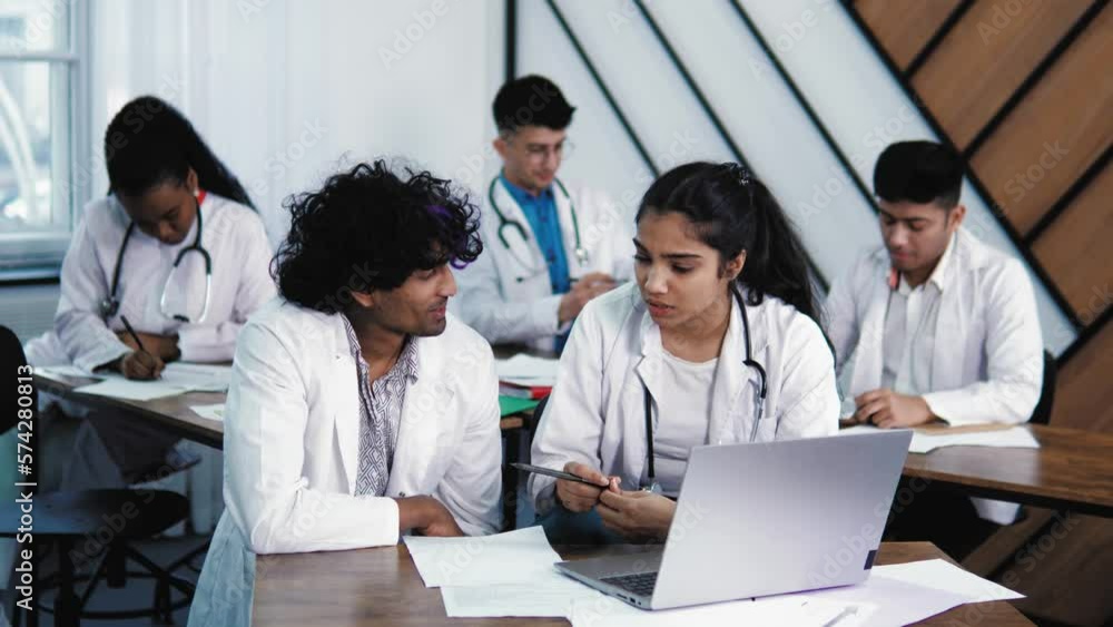 Indian medical students working on computer in public library. Diverse young people studying on laptop in college library, discussing the health result of patient consulting. Intelligent future doctor Indian medical students working on computer in public library. Diverse young people studying on laptop in college library, discussing the health result of patient consulting. Intelligent future doctor