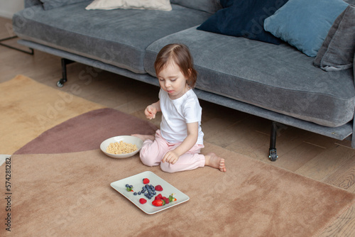 Bild auf Leinwand Two-year-old girl in pajamas eats berries