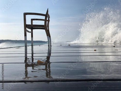 Schilderij op canvas Chaise en bois sur une jetée avec une grosse vague en arrière plan