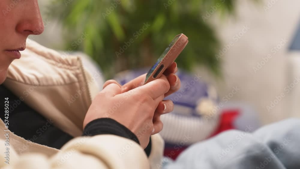 young person using and texting on mobile device in her home with plants in the background young person using and texting on mobile device in her home with plants in the background