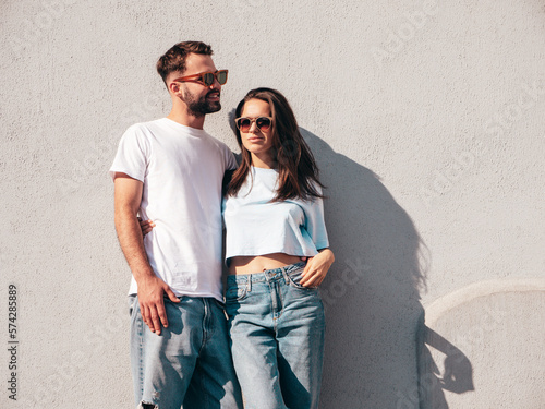 Smiling beautiful woman and her handsome boyfriend. Woman in casual summer jeans clothes. Happy cheerful family. Female having fun. Sexy couple posing in the street near wall. In sunglasses