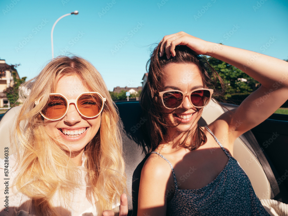 Portrait of two young beautiful and smiling hipster female in convertible car. Sexy carefree women driving. Positive models riding and having fun outdoors. Enjoying summer days. Cheerful and happy Portrait of two young beautiful and smiling hipster female in convertible car. Sexy carefree women driving. Positive models riding and having fun outdoors. Enjoying summer days. Cheerful and happy