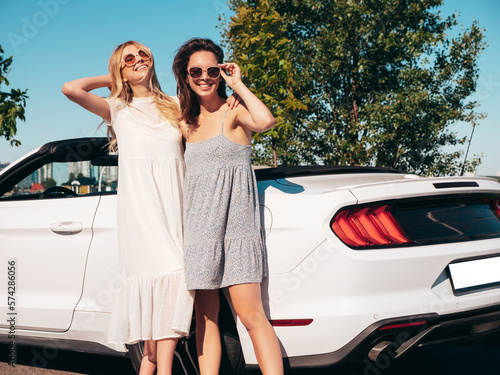 Two young beautiful and smiling hipster female in convertible car. Sexy carefree women posing near cabriolet. Positive models riding and having fun in sunglasses outdoors. Enjoying summer days © halayalex