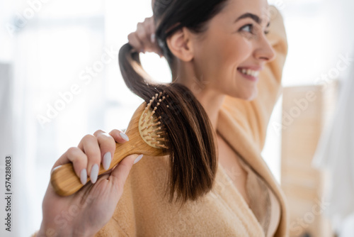 Canvas Print smiling and blurred young woman brushing shiny hair in bathroom.