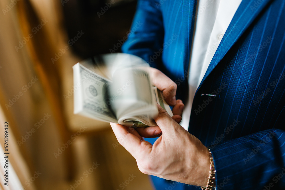 Man checking a thick stack of 100 dollar bills thumbing. Man in suit showing dollar banknotes. Hands counting money American dollars. Income. Business Success Concept.