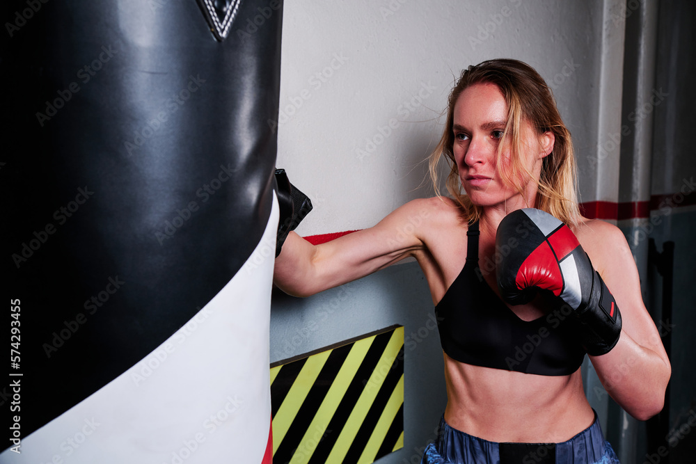 Female athlete punching the bag while training at a boxing gym.
